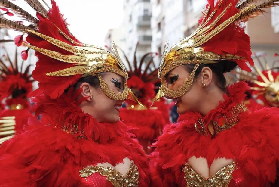 Comparsistas con tocados de plumas rojas y doradas durante el Carnaval de Águilas