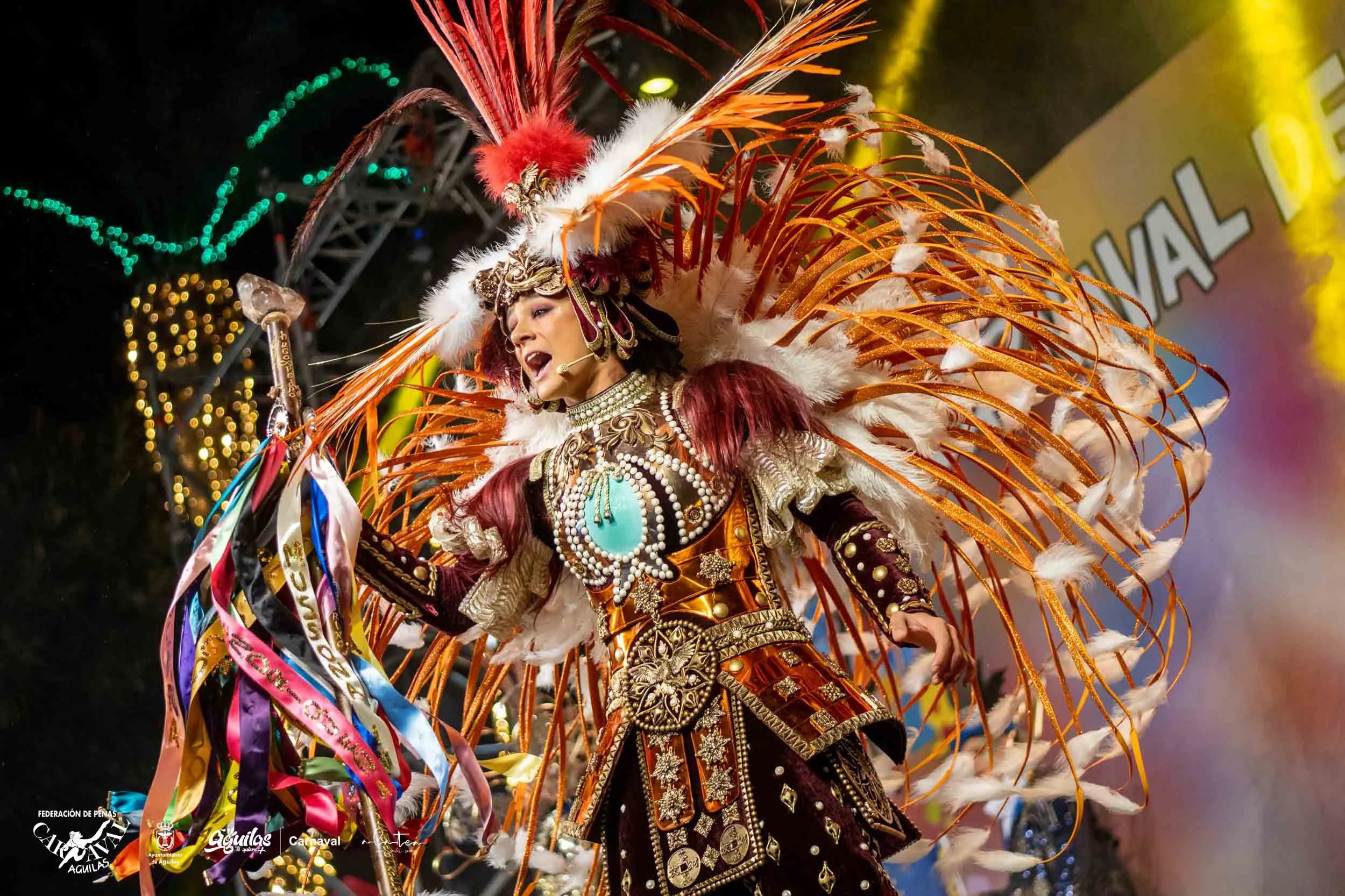 Actuación nocturna con disfraz de plumas naranjas y doradas en el Carnaval de Águilas