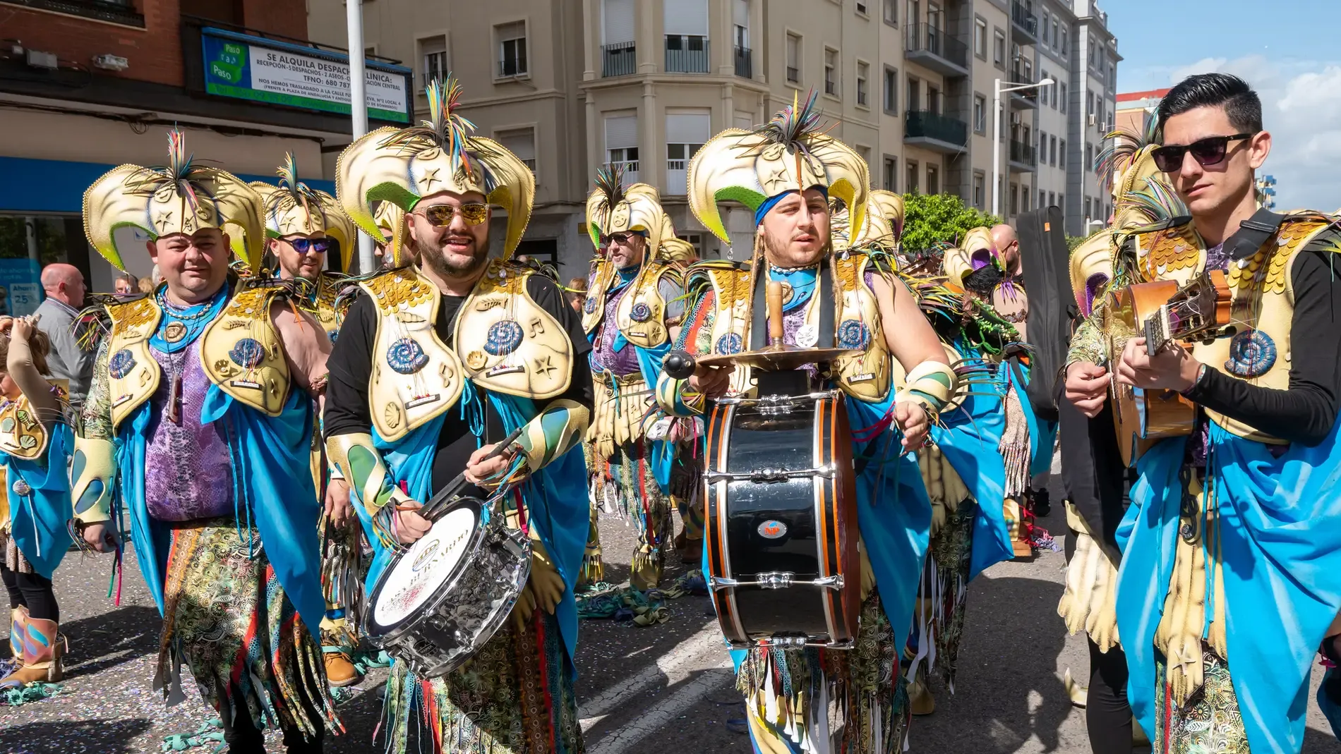 Comparsa con disfraces dorados y tambores desfilando por las calles del Carnaval de Cádiz
